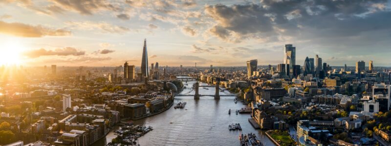 The tidal River Thames, with docked boats in the foreground, and Tower bridge, the Shard, and City skyline in the background.